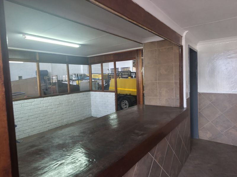 An industrial utility space featuring a built-in counter, tiled wall finishes, and an internal glass partition overlooking the warehouse area.