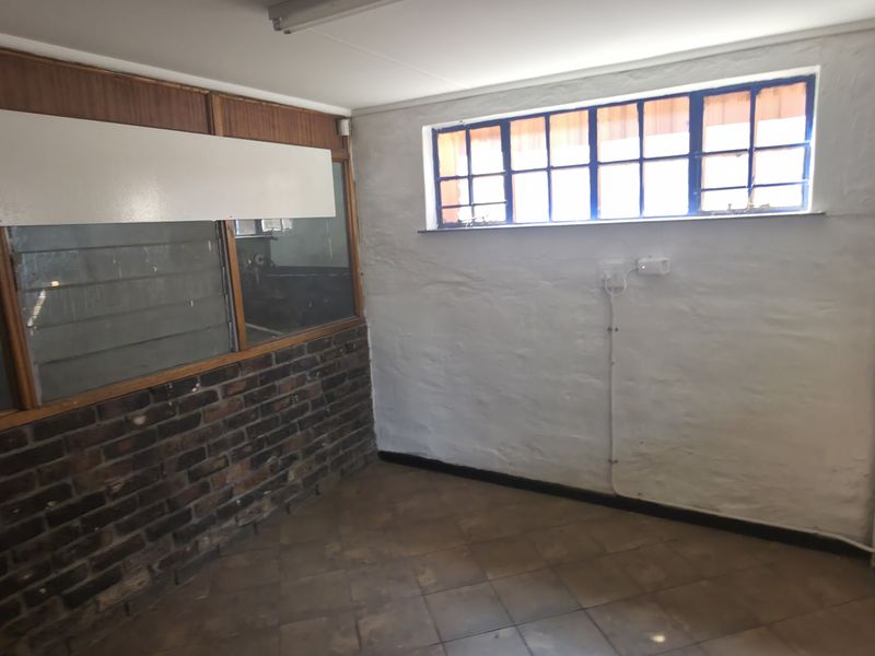 An empty industrial-style office space featuring exposed brickwork, timber-framed glass partitions, and tiled flooring, offering a functional layout for a workspace.