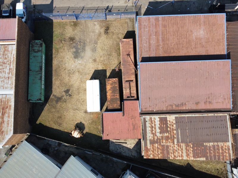 Aerial view of an industrial property featuring multiple warehouse structures with corrugated metal roofing and a fenced yard area.