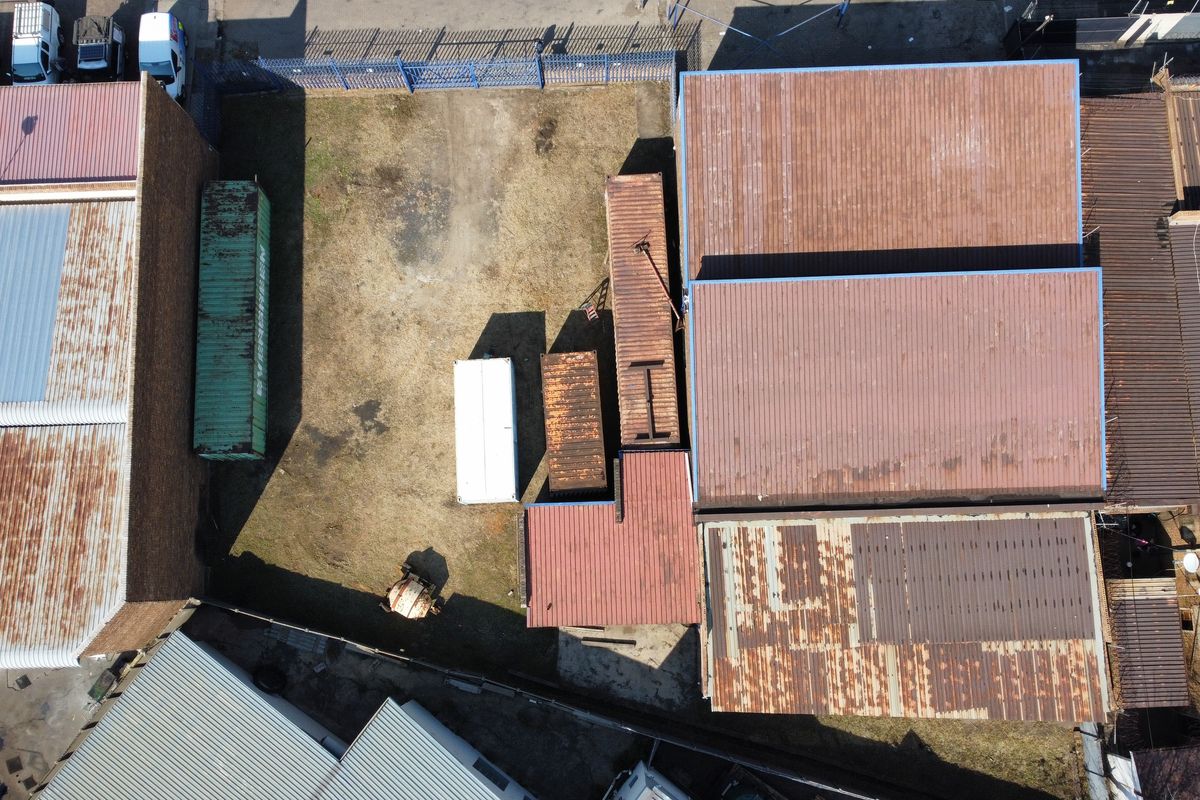 Aerial view of an industrial property featuring multiple warehouse structures with corrugated metal roofing and a fenced yard area.
