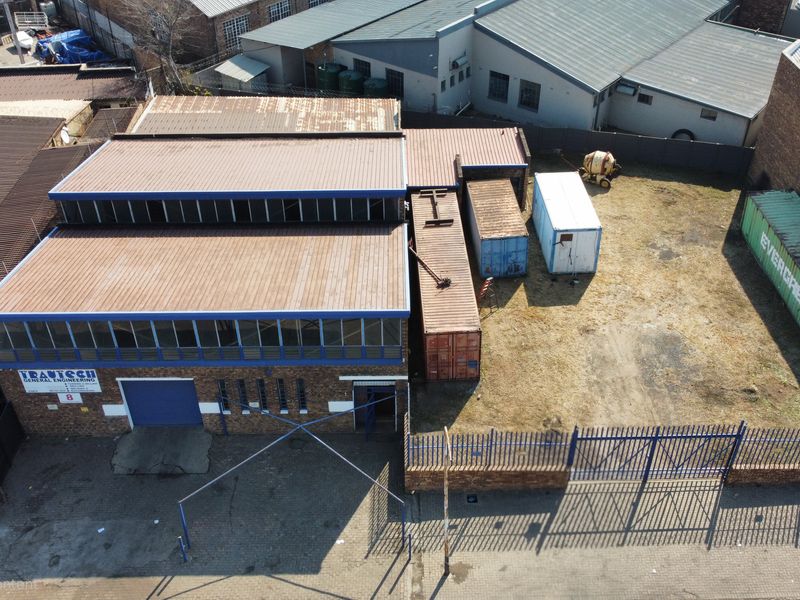 Aerial view of an industrial property featuring a brick warehouse with a corrugated metal roof, gated entrance, and an open yard area.