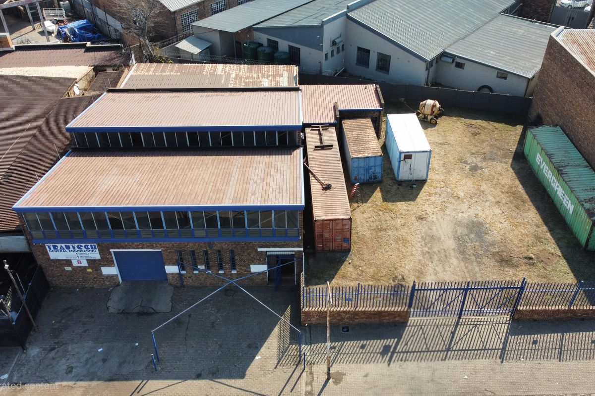 Aerial view of an industrial property featuring a brick warehouse with a corrugated metal roof, gated entrance, and an open yard area.