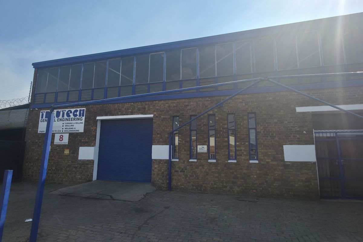 Front elevation of an industrial engineering facility featuring a brick facade, roller shutter door, and upper-level windows with security fencing.