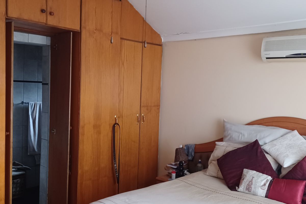 A bedroom featuring built-in wooden cabinetry, an en-suite bathroom access, and a wall-mounted air conditioning unit.