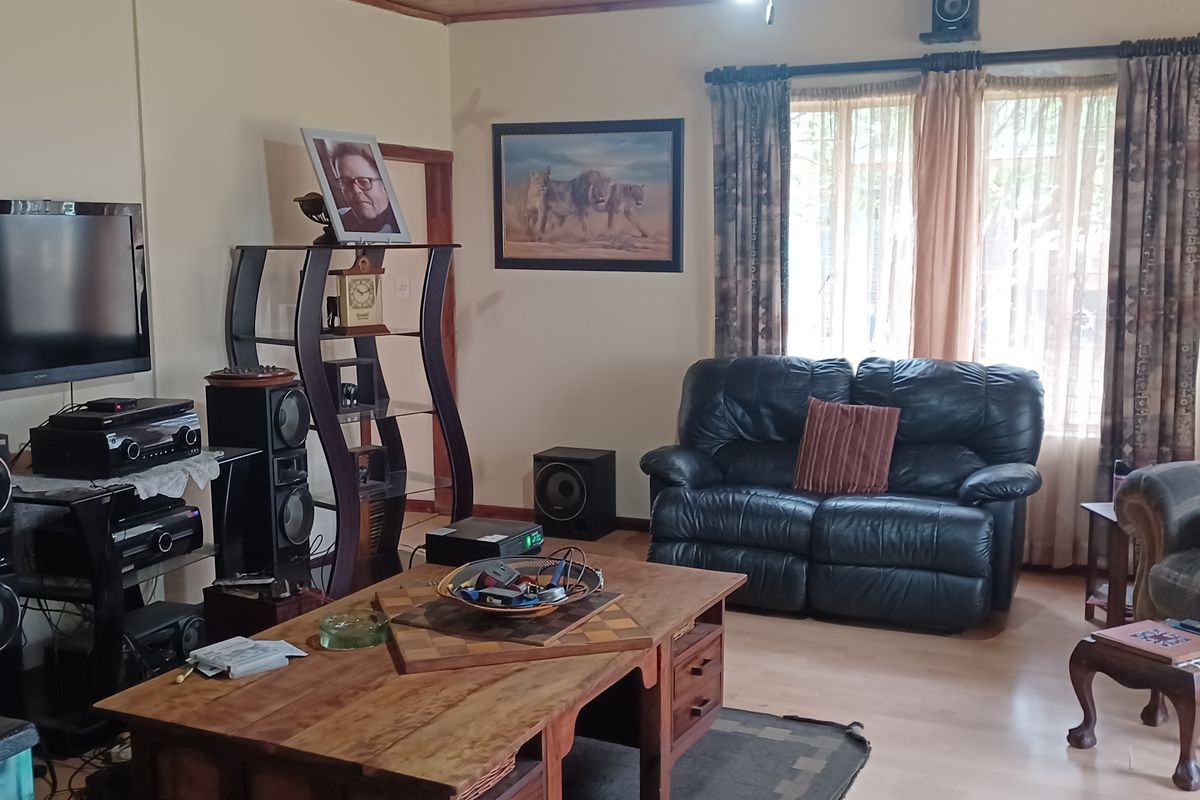 A comfortable living room featuring laminate flooring, large windows with curtains, and a neutral wall finish.