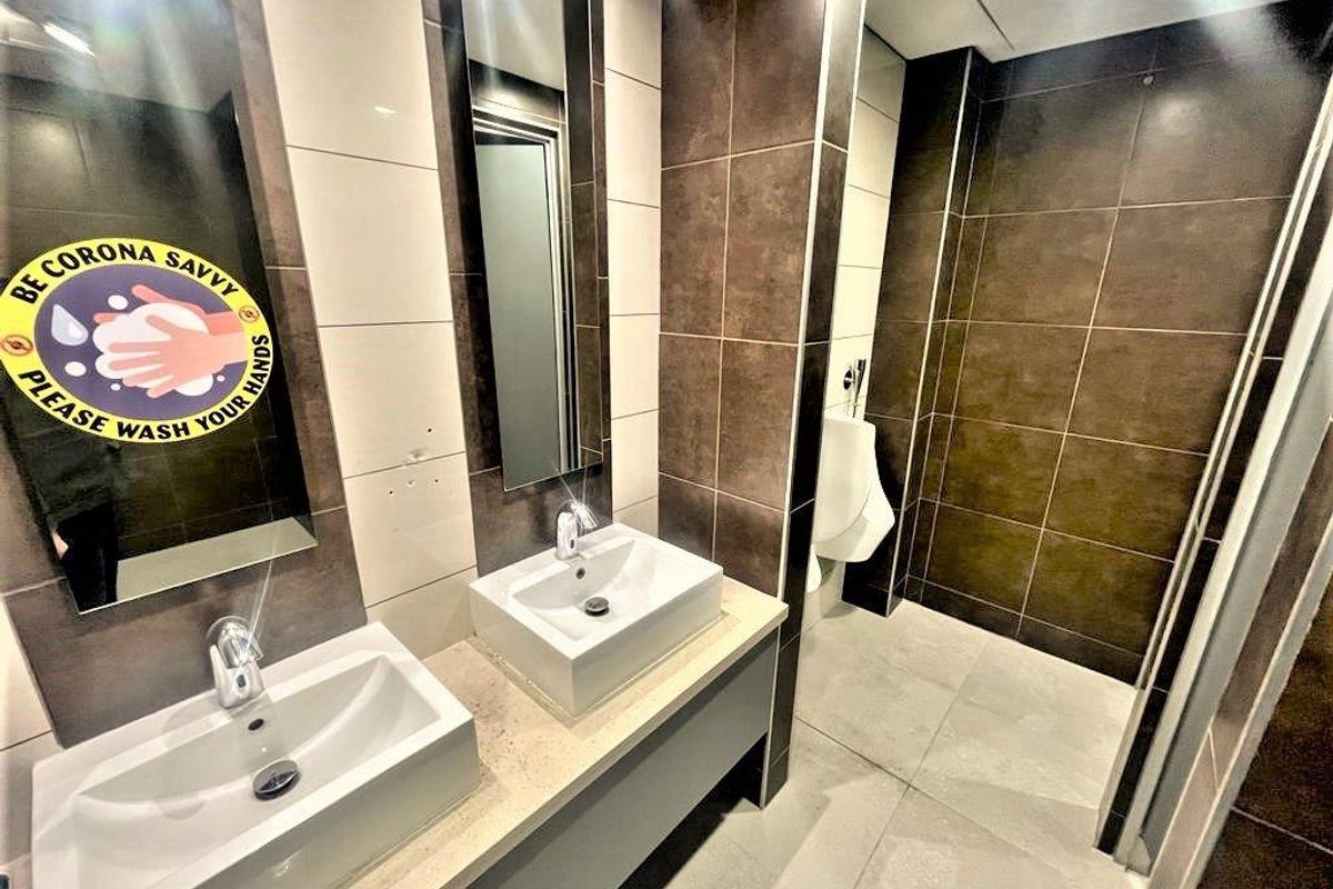 Modern office restroom featuring dual vessel sinks, stone vanity countertop, wall-mounted urinals, and contemporary dark and light tiled finishes.