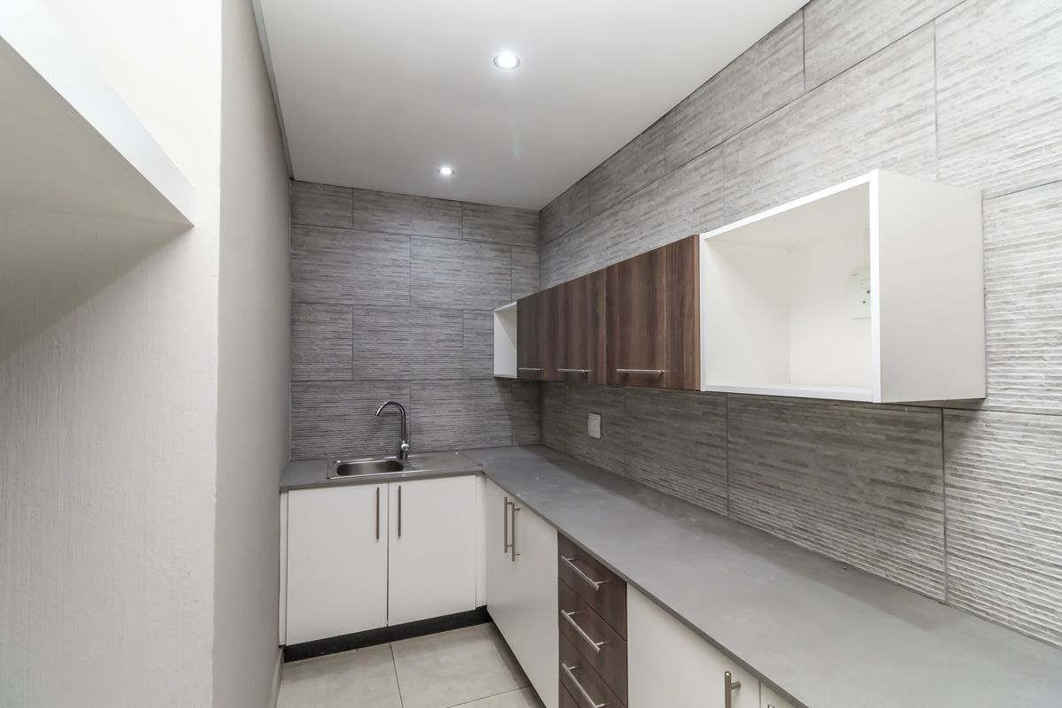 A compact, modern kitchenette featuring built-in cabinetry, a stainless steel sink, and textured grey wall tiling.