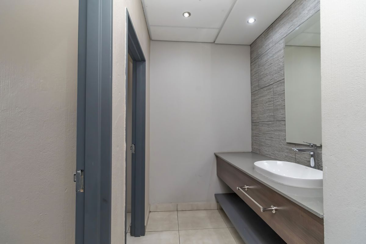 A modern office restroom featuring a sleek vanity with a vessel sink, tiled backsplash, and recessed ceiling lighting.
