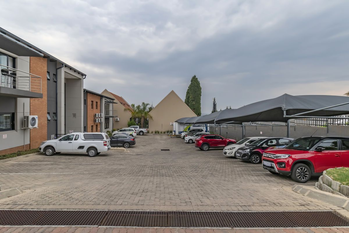A paved office parking area featuring covered shade-net parking bays and modern brick and concrete building facades.
