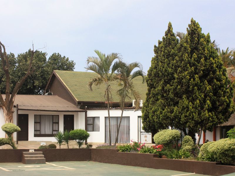 Front elevation of the property featuring a reception area, tiled roofing, and a paved driveway with established garden landscaping.