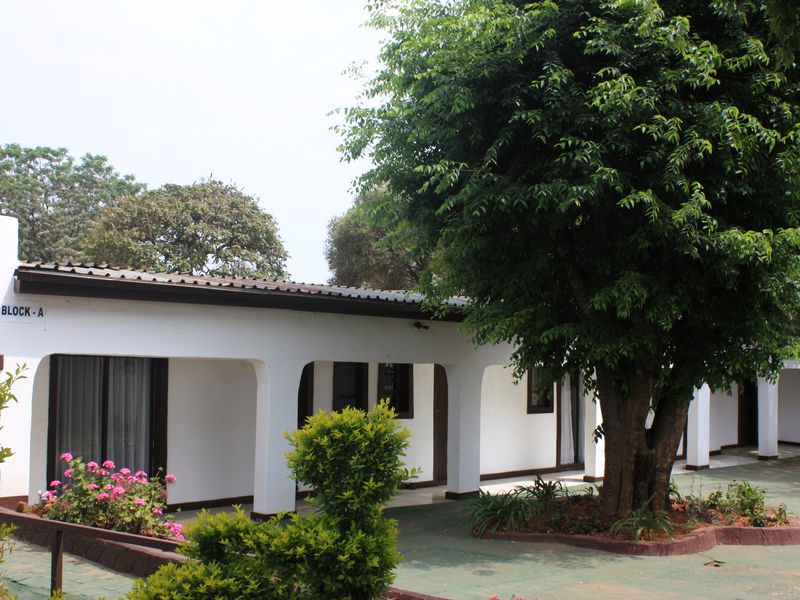 A view of the front facade of Block A, featuring a covered patio area with arched pillars and mature trees in the foreground.