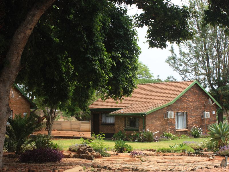 A well-maintained face-brick cottage set within a lush, landscaped garden, featuring tiled roofing and exterior-mounted air conditioning units.