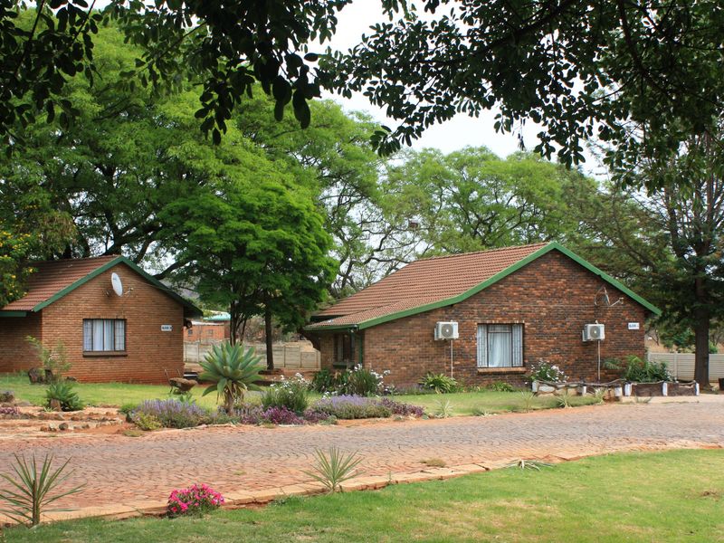 A view of two face-brick residential units on a small holding, featuring tiled roofs, paved driveway access, and established garden surroundings.