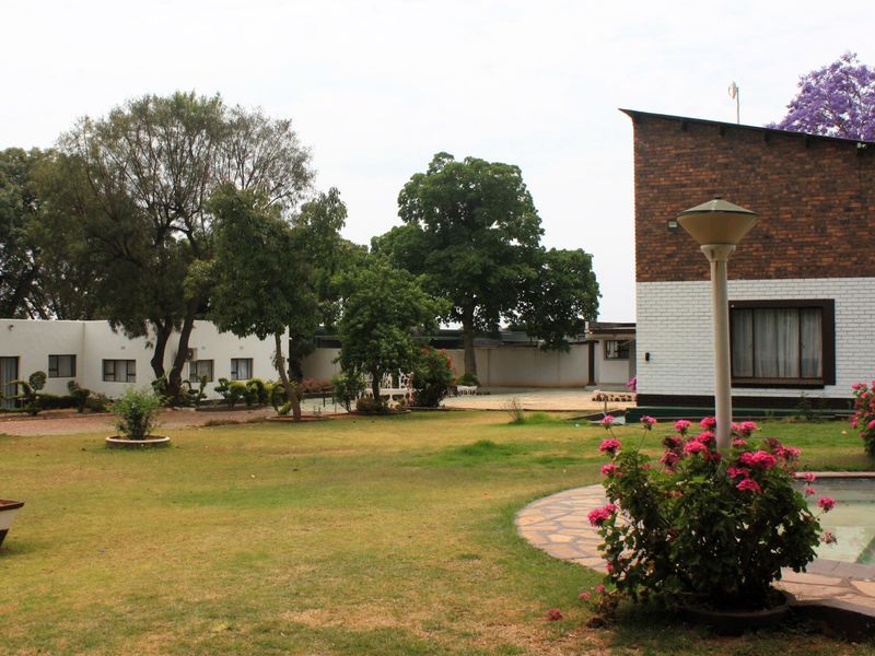 A spacious garden area featuring a swimming pool, manicured lawn, and brick-finished building exteriors on a small holding property.