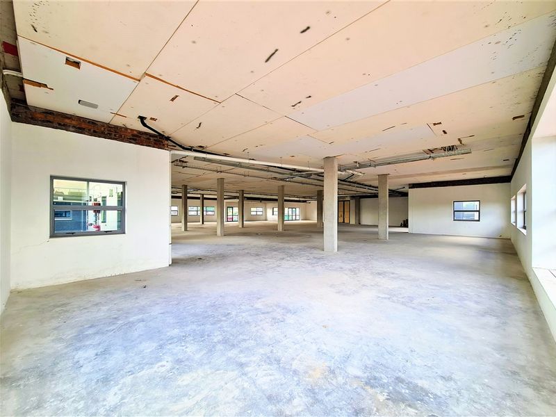 A large, open-plan office space in shell condition, featuring exposed concrete columns, unfinished ceiling panels, and expansive floor area ready for custom fit-out.