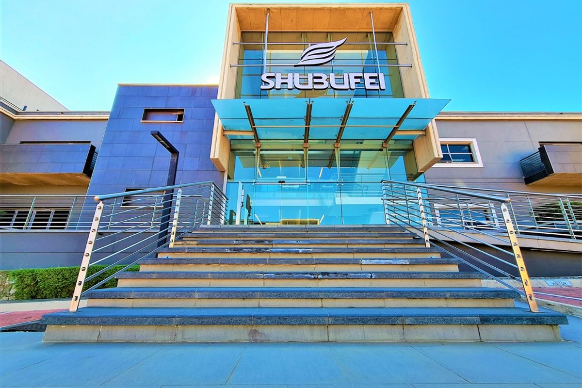 Modern office building entrance featuring a prominent glass facade, stainless steel railings, and stone steps leading to the main entry.
