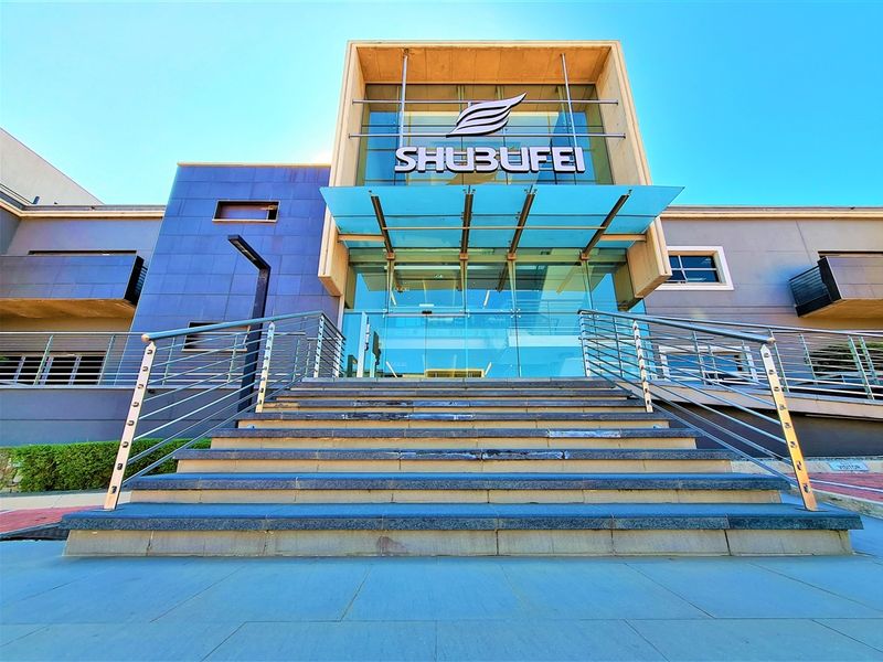 Modern office building entrance featuring a prominent glass facade, stainless steel railings, and stone steps leading to the main entry.