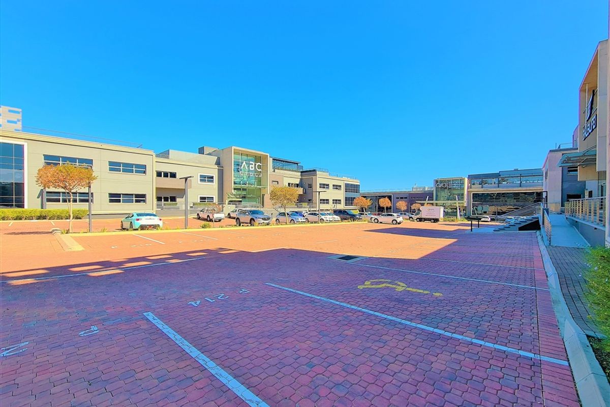 A wide-angle view of a modern commercial office complex featuring a large paved parking area and contemporary building facades with glass elements.