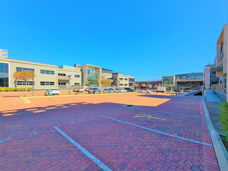 A wide-angle view of a modern commercial office complex featuring a large paved parking area and contemporary building facades with glass elements.