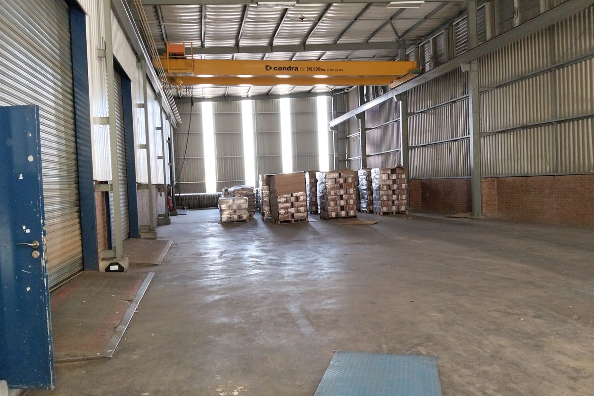 Spacious industrial warehouse featuring a high-clearance ceiling, integrated overhead crane, durable concrete flooring, and large roller shutter access doors.