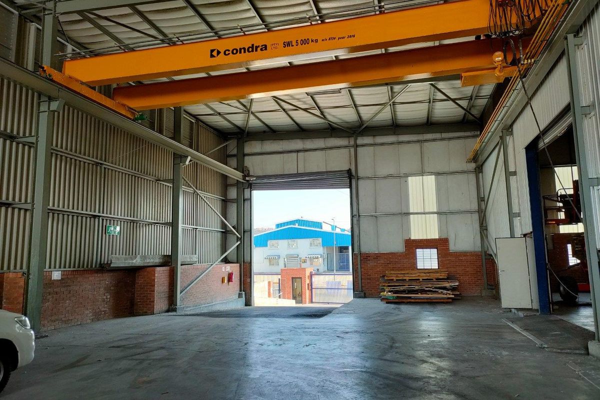 Spacious industrial warehouse unit featuring high ceilings, concrete flooring, and a heavy-duty overhead bridge crane, with large roller shutter access.