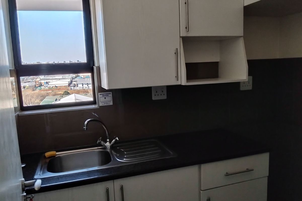 A compact kitchen area featuring white built-in cabinetry, a stainless steel sink with mixer tap, dark laminate countertops, and a window with exterior views.