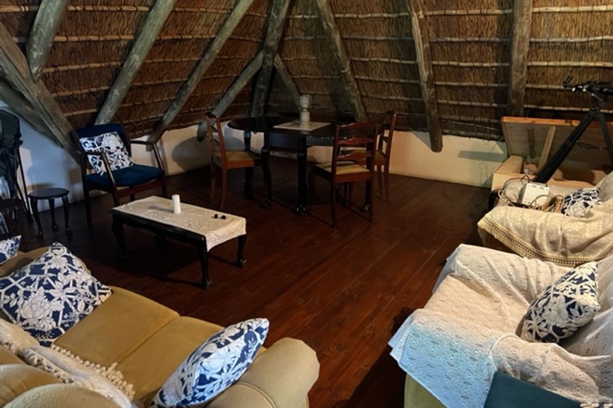 A rustic living area featuring exposed timber roof trusses, a traditional thatched ceiling, and warm timber flooring, creating a cozy farm-style atmosphere.