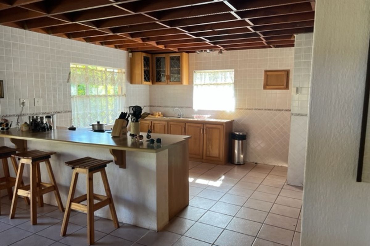 A rustic kitchen featuring exposed timber beam ceilings, tiled flooring, wooden cabinetry, and a functional breakfast bar area.