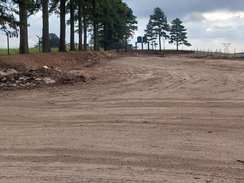 Expansive industrial land plot featuring perimeter fencing, mature trees, and elevated water storage tanks on site.