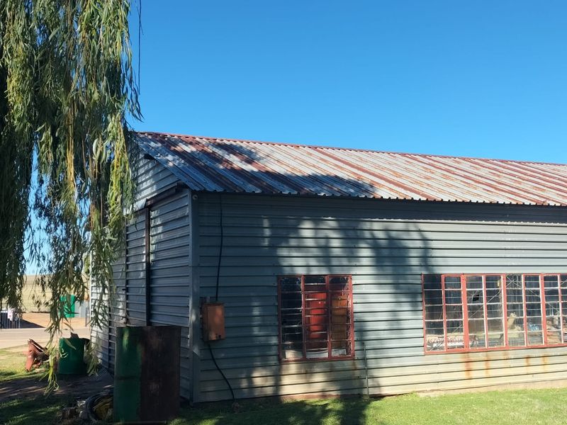 Exterior view of an industrial-style corrugated metal building featuring steel-framed windows and showing signs of significant weathering and rust on the roof and walls.