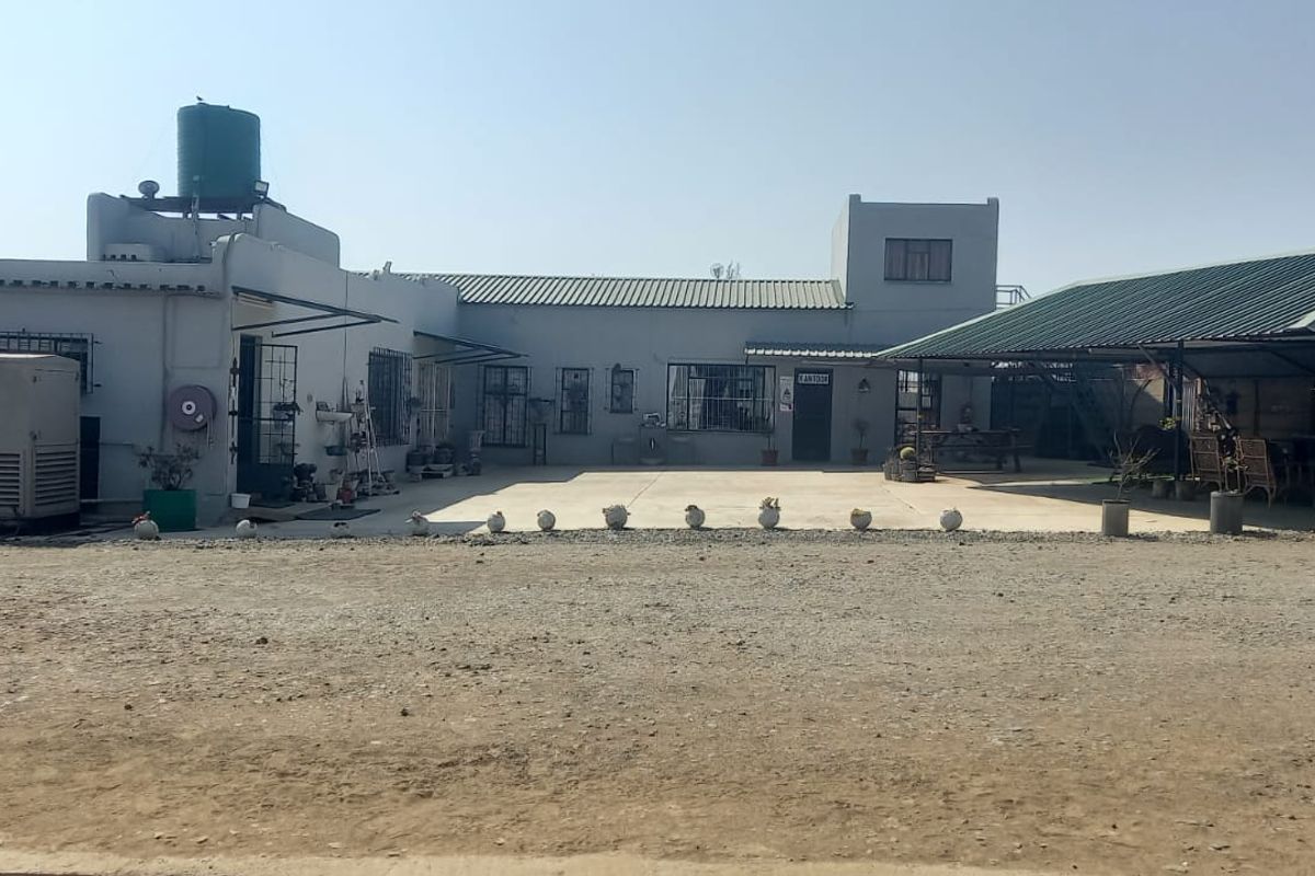 Rear exterior view of a commercial property featuring a concrete courtyard, covered patio area, backup generator, and water tank infrastructure.