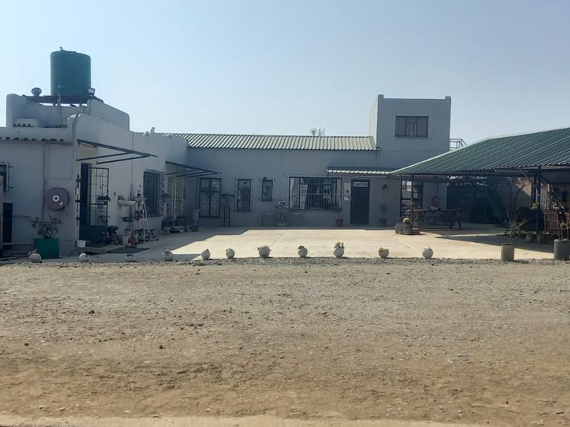 Rear exterior view of a commercial property featuring a concrete courtyard, covered patio area, backup generator, and water tank infrastructure.