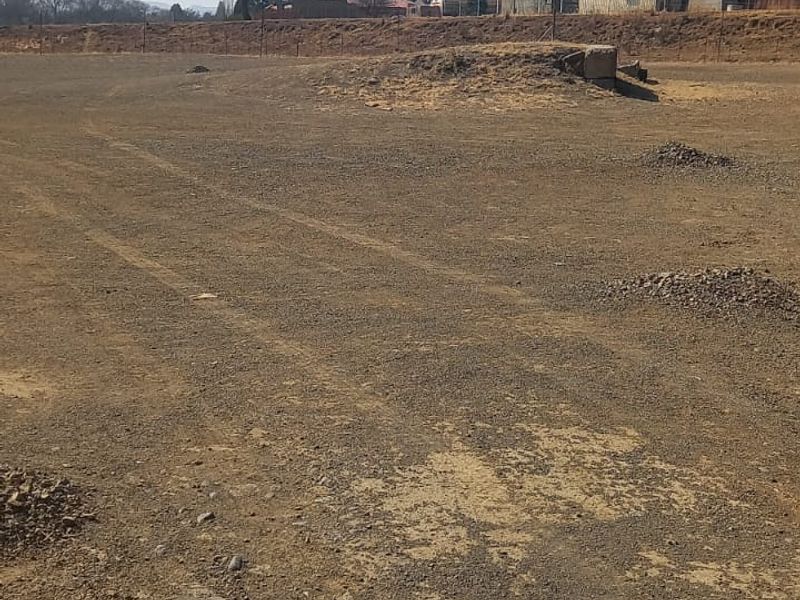 An expansive, undeveloped plot of land featuring raw earth terrain and perimeter fencing, suitable for future commercial development.