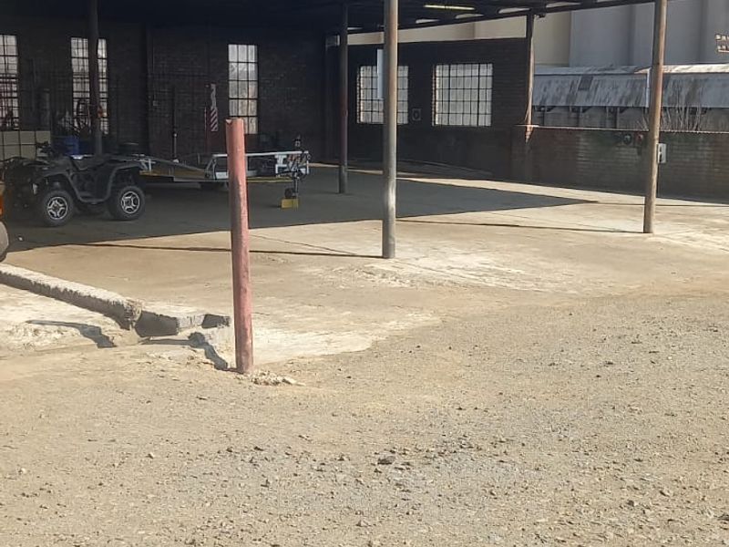 A large, open-plan industrial utility space featuring a covered concrete area, exposed brick walls, and steel-framed windows, suitable for storage or commercial operations.