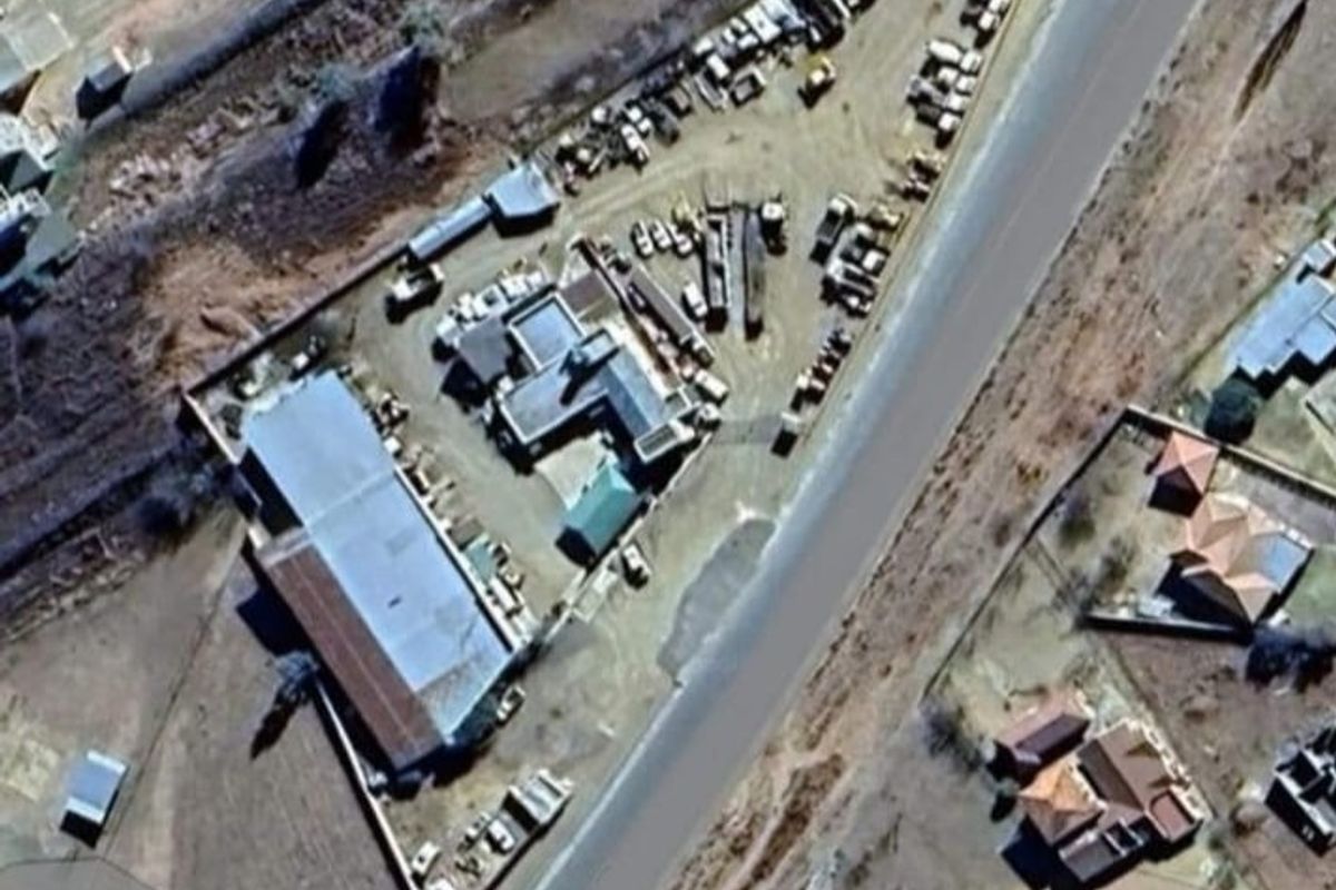 Aerial view of a commercial property featuring multiple structures, extensive yard space, and perimeter fencing with direct road access.