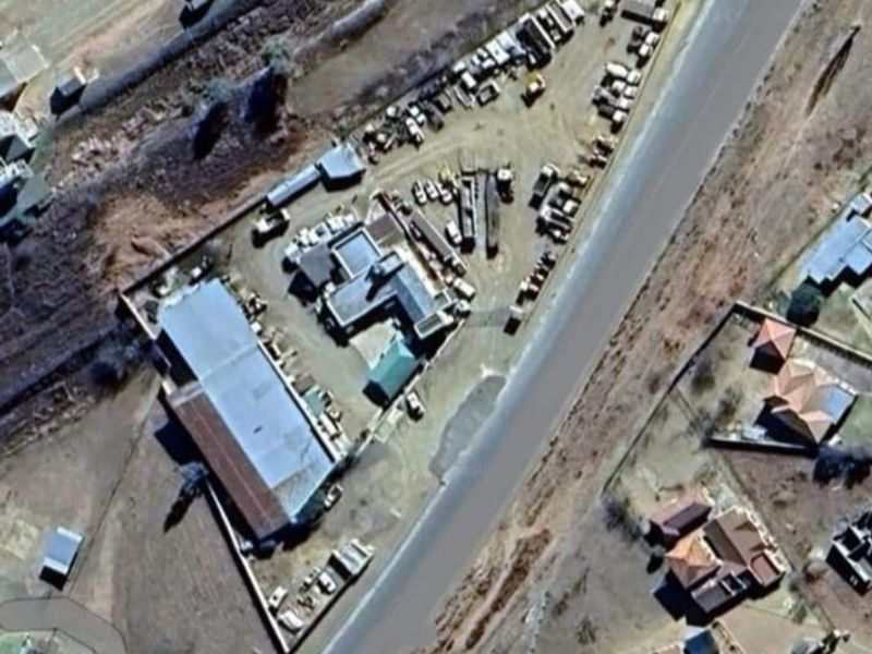 Aerial view of a commercial property featuring multiple structures, extensive yard space, and perimeter fencing with direct road access.