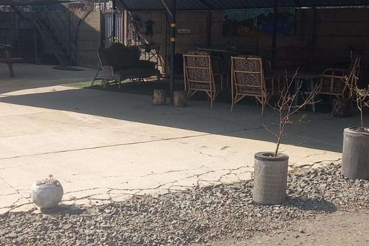 A covered outdoor patio area featuring a corrugated metal roof, steel support structure, and concrete flooring with visible surface cracking.