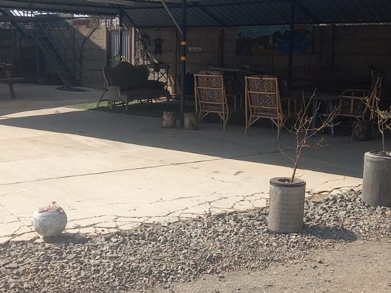 A covered outdoor patio area featuring a corrugated metal roof, steel support structure, and concrete flooring with visible surface cracking.