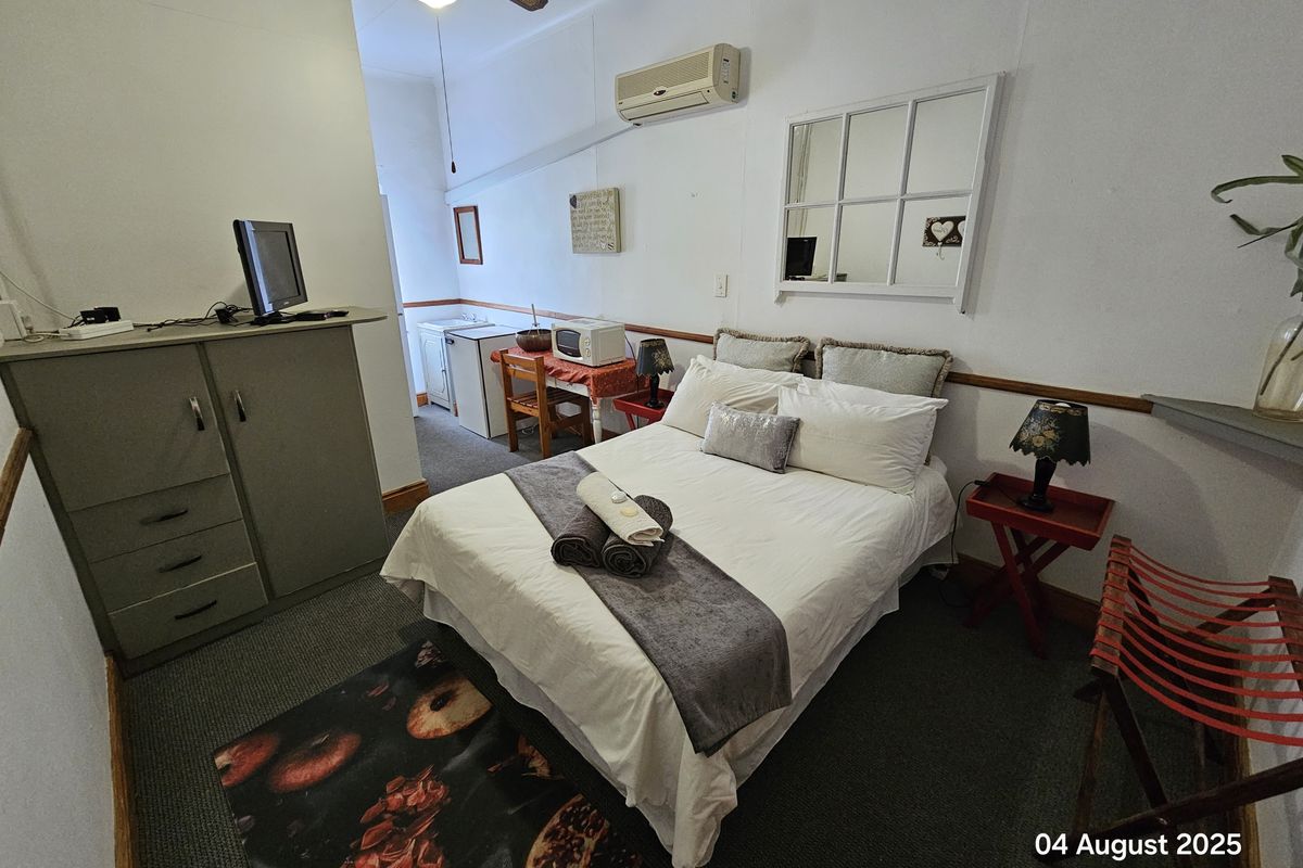 A compact hotel bedroom featuring a ceiling fan, wall-mounted air conditioning unit, and a small kitchenette area with built-in cabinetry.