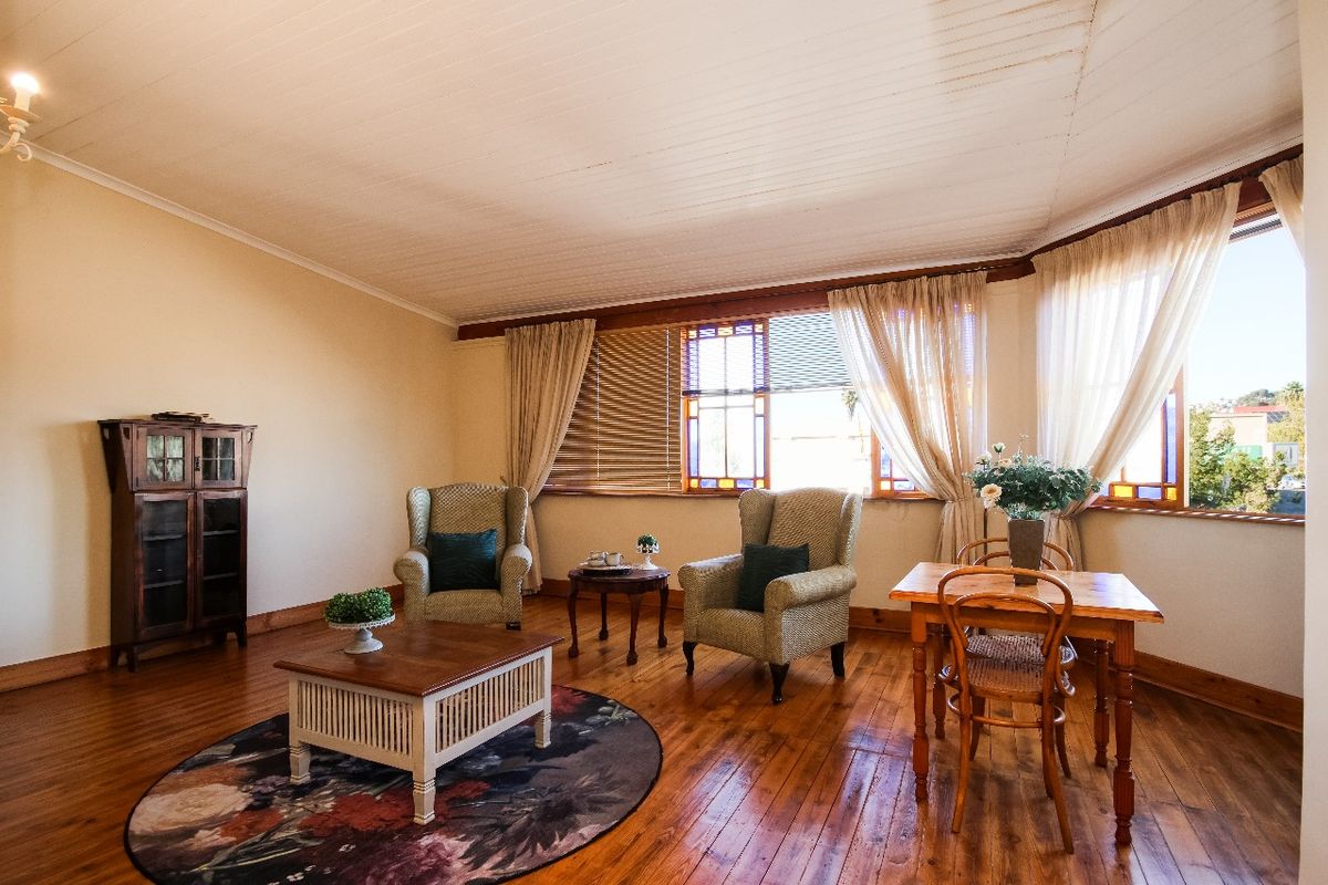 A bright living room featuring polished timber flooring, a white timber-paneled ceiling, and large windows with decorative stained glass accents.