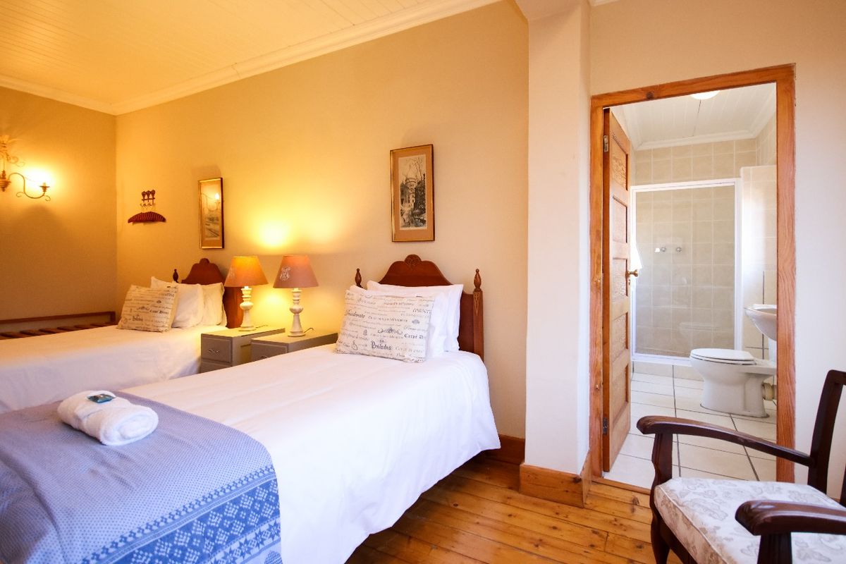 A hotel bedroom featuring timber flooring and an en-suite bathroom with a tiled shower enclosure and toilet.