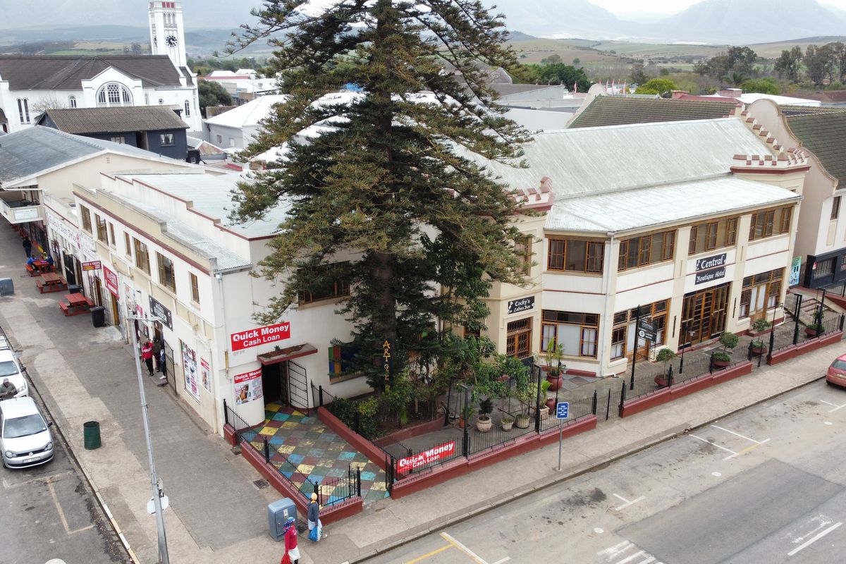Aerial view of a multi-story commercial building featuring a prominent corner location, tiled entrance courtyard, and established tree, situated in a town center.