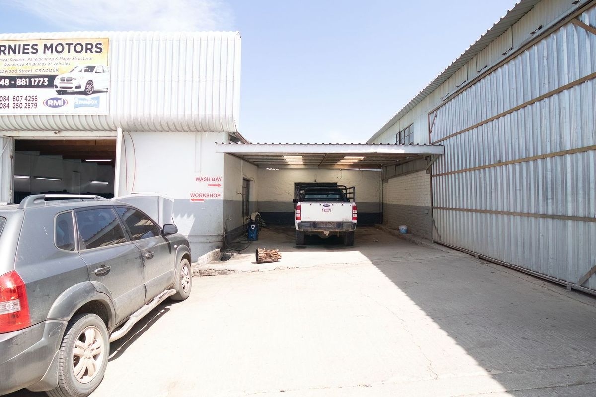Exterior view of a commercial workshop facility featuring a dedicated wash bay area, concrete driveway, and large metal-clad industrial structures.
