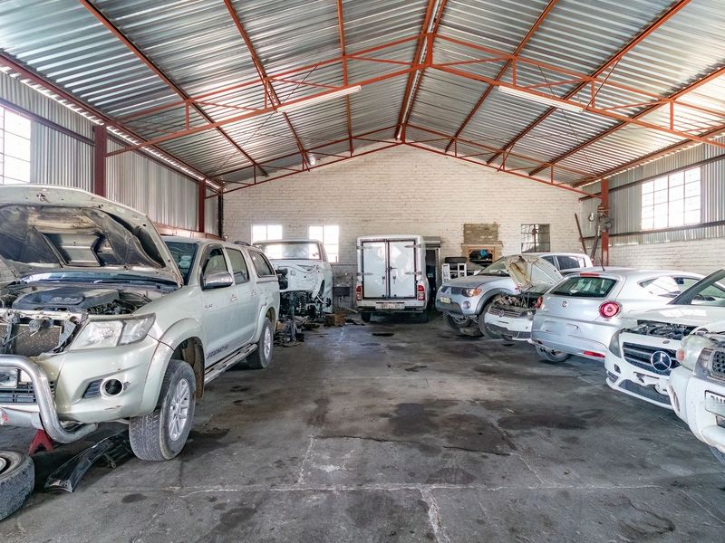 Spacious industrial workshop or garage facility featuring high-pitched corrugated metal roofing, exposed brick walls, and concrete flooring, suitable for automotive or storage use.