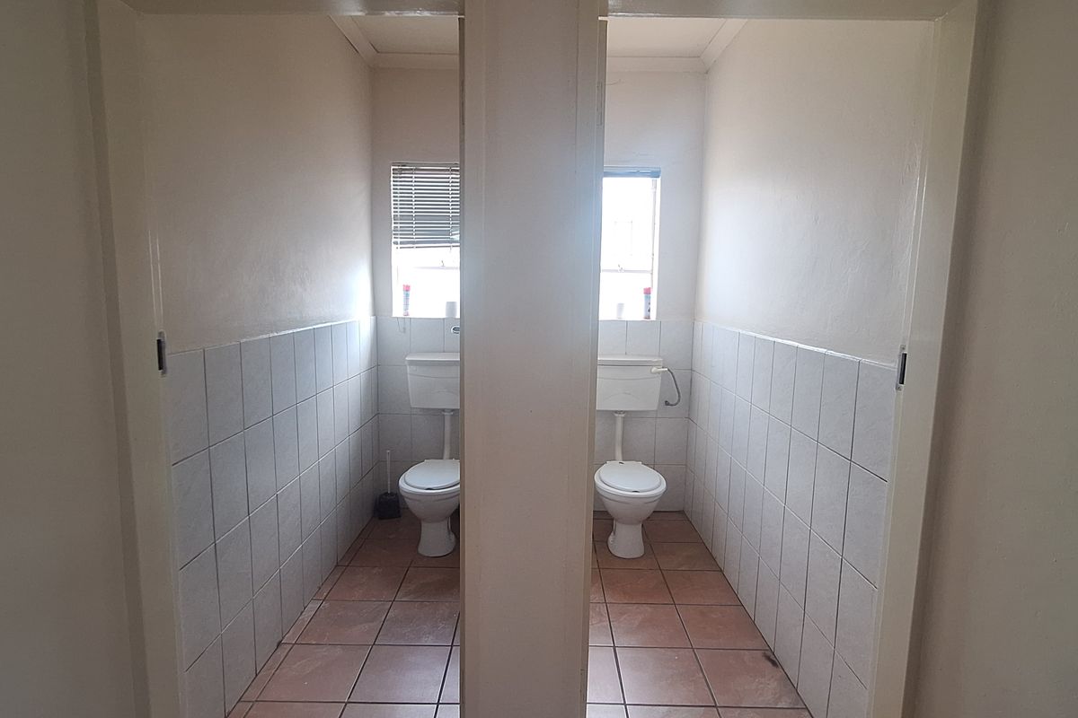 Two separate commercial restroom cubicles featuring tiled flooring, wall-mounted toilets, and privacy signage.