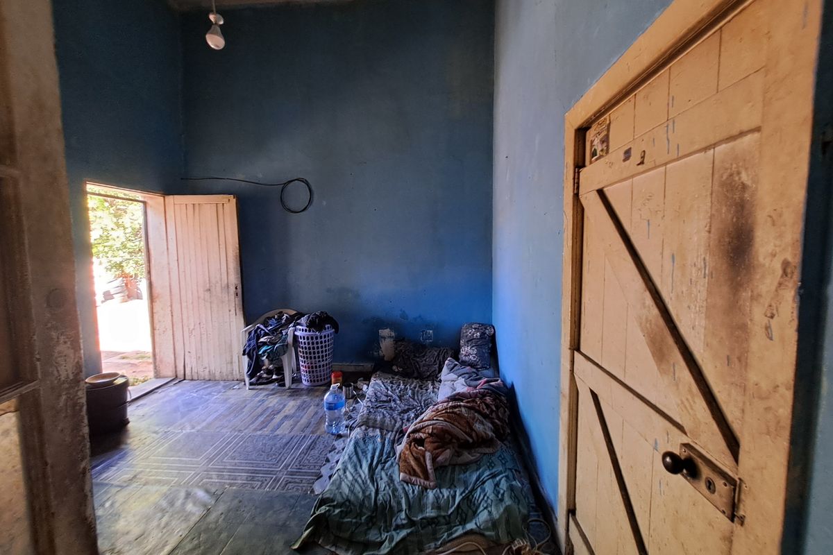 A bedroom space featuring tiled flooring and a timber door, requiring significant cosmetic updates and wall repairs to improve the overall condition.
