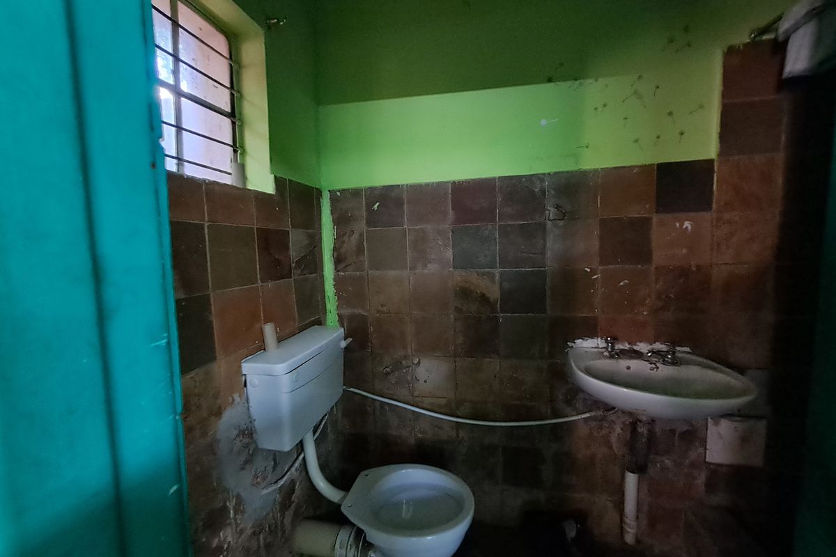 A small, dated bathroom featuring a pedestal basin, flush toilet, and tiled walls in need of renovation and cosmetic updates.