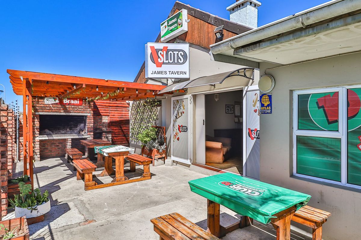 Outdoor entertainment area featuring a built-in brick braai, wooden pergola, and concrete patio space, providing a functional exterior gathering area for the tavern.