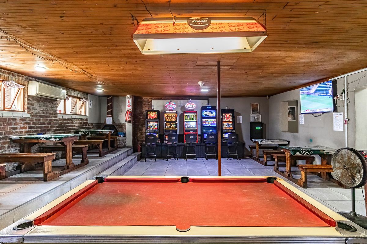 Spacious commercial bar area featuring exposed brick walls, wood panel ceiling, tiled flooring, and built-in gaming machine station.