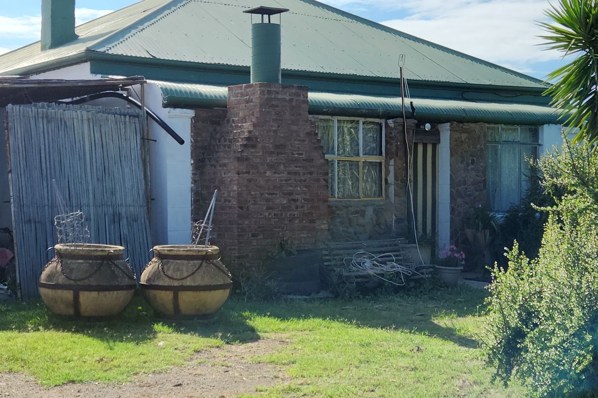Exterior view of a rustic farm cottage featuring a prominent brick chimney, corrugated metal roof, and stone-accented facade.